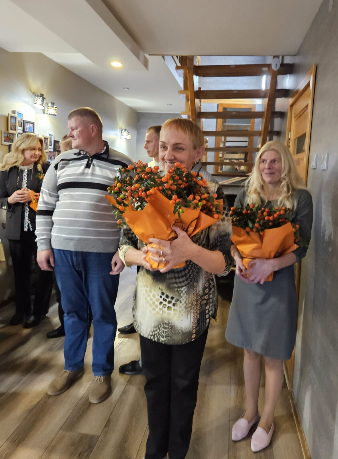 Šypsantys žmonės laiko oranžinių gėlių puokštes.
